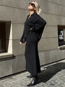 Stylish model wearing a black V-neck knit sweater and matching long skirt set outdoors.