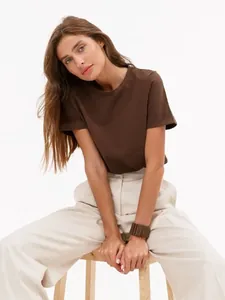 Ganzkörperaufnahme einer Frau in einem braunen Rundhals-T-Shirt und einer beigen Hose