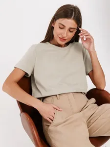 Frau im lässigen khakifarbenen Kurzarm-T-Shirt auf einem Stuhl für einen entspannten Look