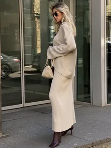 Full-length side view of a minimalist beige knit sweater and maxi skirt set on a model in city