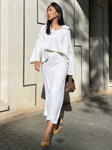 Detail of white knit two-piece set with V-neck sweater and midi skirt on model.