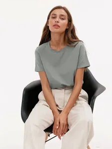 Professionelle Aufnahme einer Frau in einem grauen T-Shirt mit Rundhalsausschnitt auf Stuhl.