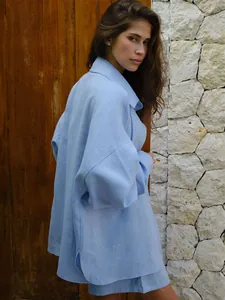 Woman wearing a casual light blue long-sleeved linen shirt and shorts set in a rustic setting.