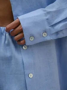 Detailed view of a light blue linen-textured shirt sleeve with pearlescent buttons.