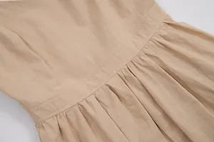 Close-up of beige cotton linen dress fabric texture and pleated waistline details.