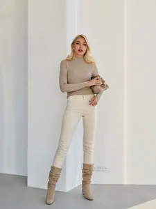 Full shot of a model in a slim-fit beige mock neck ribbed knit sweater with cream pants.