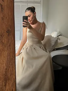 Elegant beige cotton V-neck camisole dress with tie-shoulder straps in a bedroom setting