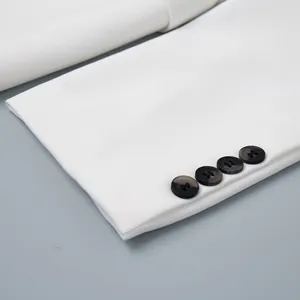 Dettaglio di quattro bottoni scuri screziati sul polsino di un blazer bianco da donna