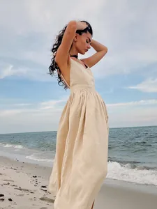 Detail of beige cotton V-neck backless maxi dress in a serene beach setting.