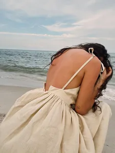 Artistic back detail of an elegant beige linen backless spaghetti strap dress at beach