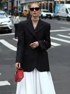 Foto street style di una donna che indossa un blazer nero sciancrato e una gonna bianca