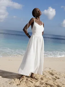 Detail view of an elegant white cotton V-neck tie-back maxi dress on a sunny beach background