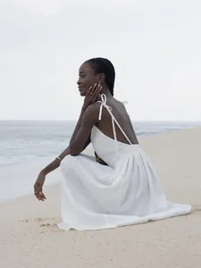 Detail view of an elegant white cotton V-neck backless sundress worn on a sandy beach