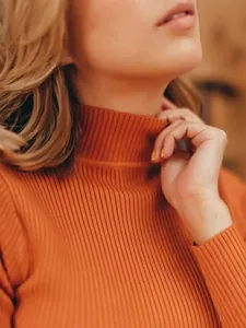 Close-up detail of the soft ribbed knit texture on a terracotta orange turtleneck sweater