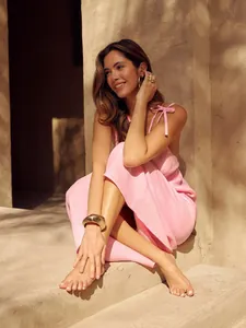 Elegant model wearing a pink V-neck backless dress in a warm sunlit architectural setting.