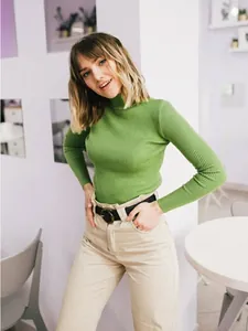Model wearing a lime green ribbed turtleneck sweater with beige trousers in a cafe setting