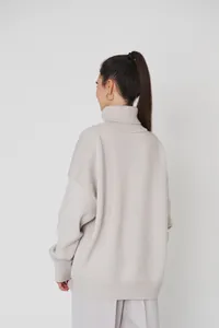 Detaillierte Rückansicht eines beigen Oversized-Rollkragenpullovers mit Strickstruktur.