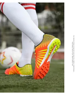 Close-up of vibrant orange soccer cleats with non-slip studs on a green grass field