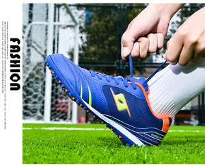 Detail of professional blue TF turf soccer shoes being tied on a grass field