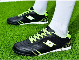 Professional black and neon green turf soccer cleats shown on artificial grass field
