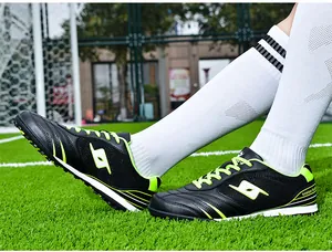 Close-up of black and neon green professional TF soccer shoes on green turf.