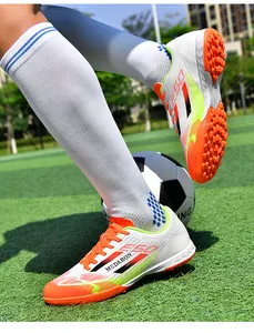 Vibrant white and orange turf soccer shoes worn on a green pitch for training.