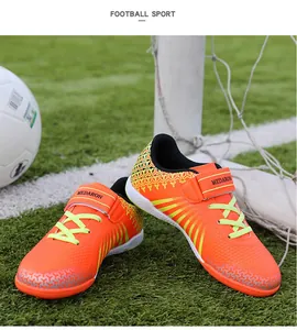 Professional children's turf soccer shoes in vibrant orange on a grass field