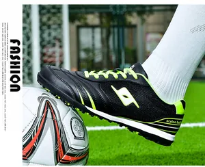 Detailed side view of professional black and neon green TF turf soccer shoes on grass