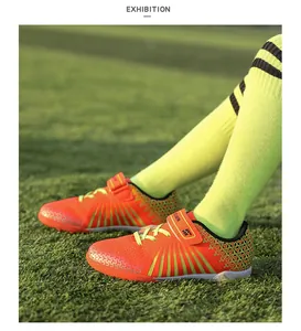Close-up of vibrant orange children's turf soccer shoes on green artificial grass