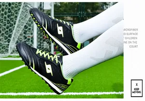 Close-up of black and neon green TF turf soccer shoes for kids on outdoor field