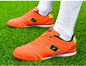 Professional orange turf soccer shoes for men shown on artificial green grass field