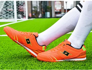 Side view of professional orange turf football shoes with black logo and cleats