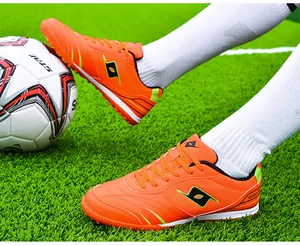 Close-up of vibrant orange turf football shoes on green artificial grass field.