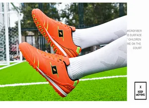 Close-up of professional orange TF soccer shoes on a green turf field with white socks