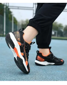 Detailopname van de zwart-oranje meisjes badmintonschoenen op een buitenveld.