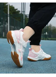 Close-up van roze-witte jeugd badmintonschoenen met rubberen zool op sportveld.