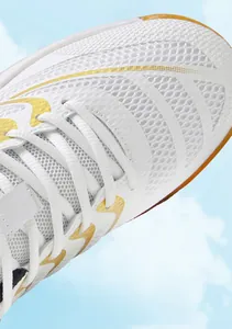 Detailopname van witte ademende badmintonschoen met gouden accenten