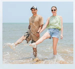 Glückliches Paar mit atmungsaktiven Wasserschuhen, das in den Meereswellen am Strand spielt.
