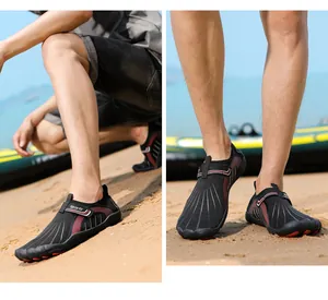 Close-up view of black outdoor water shoes with red accents worn by a person on a sandy beach