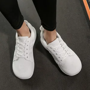 Detailed top view of white barefoot training shoes featuring wide toe box on a gym floor mat