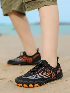 Detail view of children's non-slip aqua shoes with wing pattern on a beach.