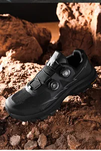Close-up of black mountain biking shoes with dual rotary dial lacing system on rocky ground.