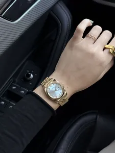 Close-up of luxury gold quartz watch with fluted bezel and pearl dial on wrist.