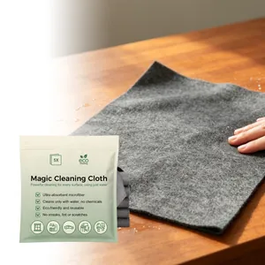 Detail view of grey Magic Cleaning Cloth wiping water on wood next to its eco packaging.
