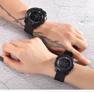 Macro detail shot of two TOMI black sports digital watches worn on tattooed wrists outdoors