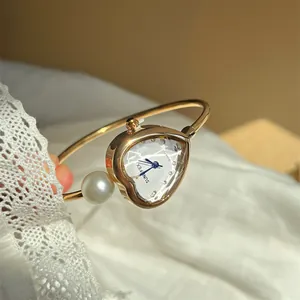 Elegant detail of a gold heart-shaped bangle watch featuring a large pearl accent
