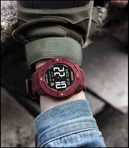Close-up of SMAEL men's sports digital watch with burgundy strap on a wrist outdoors.