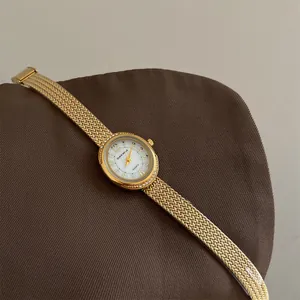 Close-up of a gold luxury quartz bracelet watch with rhinestone bezel on a textured surface