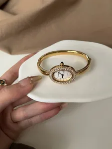 Nahaufnahme einer eleganten goldenen ovalen Armreif-Uhr mit einer Strass-besetzten Lünette