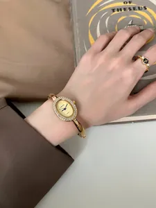 Detailansicht der goldenen ovalen Armreif-Uhr mit einer mit Strass besetzten Lünette.